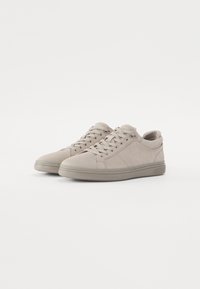 Adidași din suede gri deschis, cu vârful rotunjit, talpa plată din cauciuc și un design subțire cu șireturi, având cusături minime și o textură netedă.