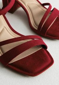 Sandali con tacco in suede rosso, dotati di tre cinturini incrociati. Design con punta quadrata, insole liscia beige e tacco impilato.
