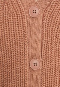 Sweter kardigan w jasnym pomarańczowym kolorze, z dekoltem w serek, dwoma dużymi guzikami oraz prążkowaną fakturą z wyraźnym przeszyciem.