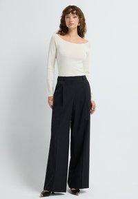 Off-white lange mouw top gecombineerd met wijde zwarte broek. De broek heeft een hoge taille en is gemaakt van een gladde stof.