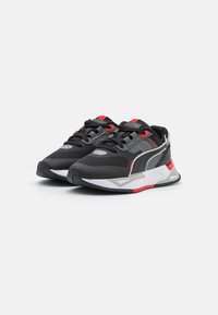 Baskets de sport noires avec des maillages et des superpositions en synthétique, présentant des accents gris, des détails rouges et une semelle blanche rembourrée.