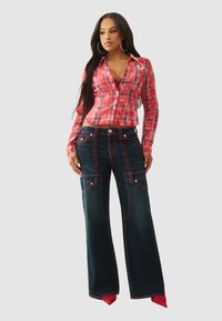 Czerwona koszula w kratę na guziki o dopasowanym kroju, zestawiona z ciemnymi dzwonowatymi spodniami dżinsowymi z czerwonym przeszyciem i dużymi przednimi kieszeniami.