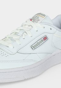 Λευκό αθλητικό παπούτσι Reebok Classic με κορδόνια, υφασμένο πέλμα και λογότυπο με τη βρετανική σημαία στο πλαϊνό πάνελ.
