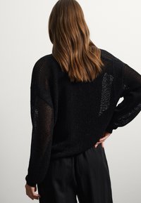 Suéter negro de punto con tejido suelto, mangas largas y un ajuste relajado. Combinado con pantalones negros que presentan un diseño texturizado.