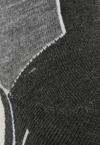 Nahaufnahme eines schwarz-grauen Strickstoffs mit sichtbaren Maschen und kontrastierenden strukturierten Mustern.