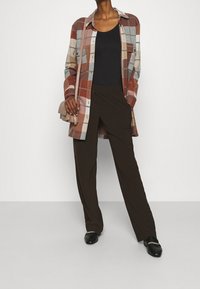 Rutig flanellskjorta i röd, brun och blå nyanser, tillsammans med en svart linne och bruna vida byxor. Liten beige handväska och svarta skor.