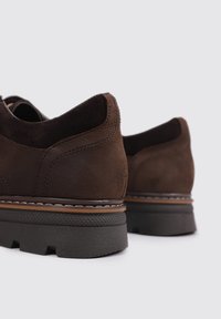 Zapatos de ante marrón con parte trasera redondeada, suela de goma texturizada, costuras en contraste y un diseño de bajo perfil.