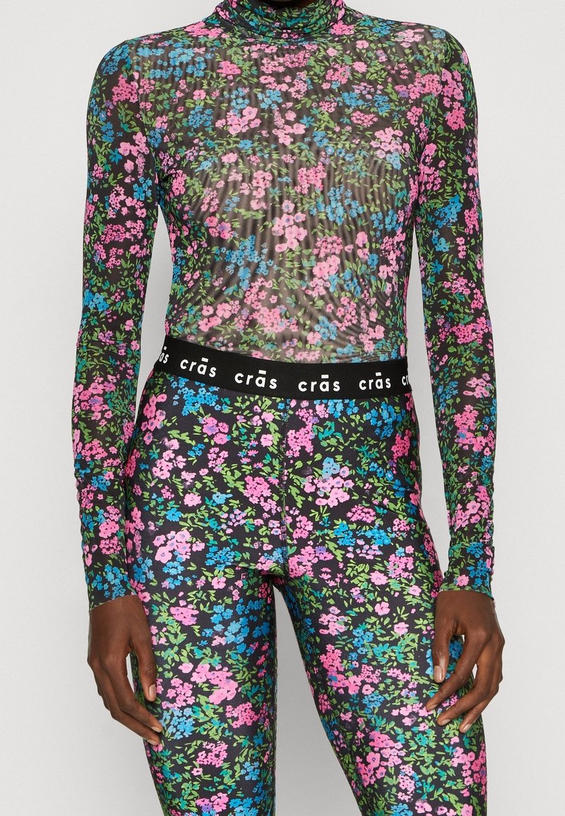 Langærmet blomster bodysuit og matchende leggings. Gennemsigtigt sort materiale med flerfarvede rosa, blå og grønne blomster mønstre. Elastisk talje.