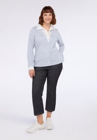 Cardigan grigio chiaro con scollo a V e bottoni, abbinato a una camicia bianca e pantaloni cropped scuri, completato da sneakers bianche.