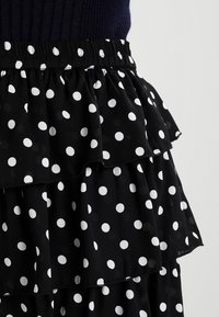 Mustat frillihameet valkoisilla pilkuilla, joissa on kerroksellisia tasoja ja joustava vyötärö. Kankaan näyttää olevan kevyt ja valuva.