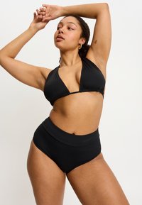 Bikini noir avec un haut à encolure halter et un détail froncé, ainsi qu'un bas taille haute. Tissu lisse et extensible avec un design minimaliste.