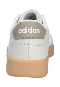 White leather sneaker with beige accents, textured back, and tan rubber sole. Features "adidas" logo prominently displayed.