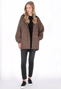 Leopárdmintás kapucnis dzseki barna és fekete színekben, rugalmas mandzsettákkal, cipzáras elülső résszel, fekete szűk farmerrel és fekete tornacipővel párosítva.