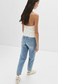 Top blanc sans manches et jean taille haute bleu clair, en coton, coupe décontractée, associé à des baskets beiges et des chaussettes blanches mi-mollet.