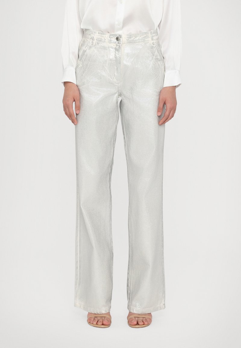 Pantalons larges en métal argenté avec une texture lisse, poches avant et fermeture à bouton, associés à un chemisier blanc.