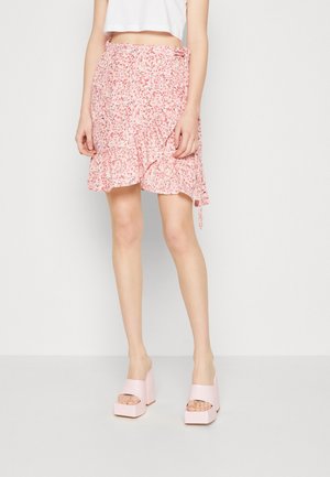 Jupe portefeuille florale rose avec ourlet volanté et détail à nouer, assortie à des sandales à talons épais rose clair. Tissu lisse avec un motif délicat.
