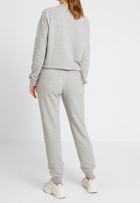 Grå sweatshirt och sweatpants-set, tillverkat av mjukt tyg. Ribbad mudd och midja, med en avslappnad passform. Vita sneakers fulländar looken.