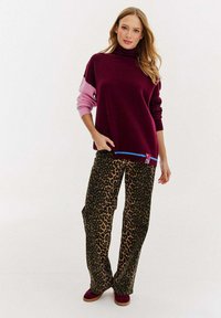 Burgundowa sweter z golfem z różowymi rękawami, połączony z szerokimi spodniami w panterkę. Akcentowany niebieskimi obszyciami i czerwonymi detalami.