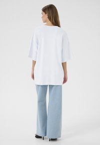Witte oversized t-shirt met korte mouwen, gladde textuur en losse pasvorm, gecombineerd met lichtblauwe wijde jeans.