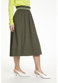 Falda midi verde oliva con cinturilla elástica y volantes, con rayas en negro y verde contrastantes. Combinada con tacones slingback blancos.