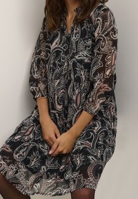 Black and pink paisley-patterned dress, sheer fabric, long sleeves, button-up front, relaxed fit, knee-length, with gathered details at the waist.