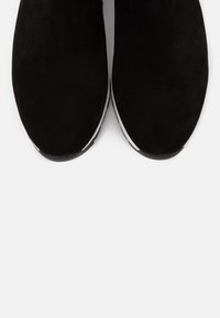 černé semišové kotníkové boty s jemnou strukturou, kulatou špičkou, bílými akcenty na podrážce a hladkým povrchem, z pohledu shora.