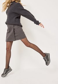 Pull en maille grise avec texture côtelée, jupe grise avec un léger éclat, et baskets grises avec semelles noires, dotées de lacets et d'accents latéraux.