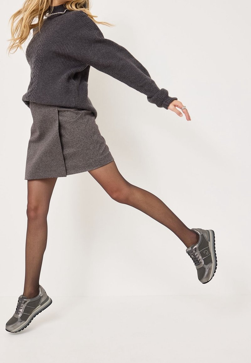 Pull en maille grise avec texture côtelée, jupe grise avec un léger éclat, et baskets grises avec semelles noires, dotées de lacets et d'accents latéraux.