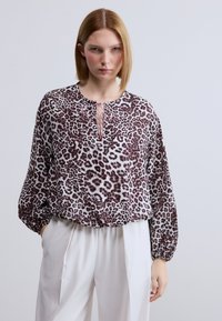 Μπλούζα με animal print λεοπάρ σε μαλακό ύφασμα, με στρογγυλή λαιμόκοψη και λεπτομέρειες με φιόγκο, μακριά μανίκια και άνετη γραμμή, συνδυασμένη με λευκό παντελόνι.