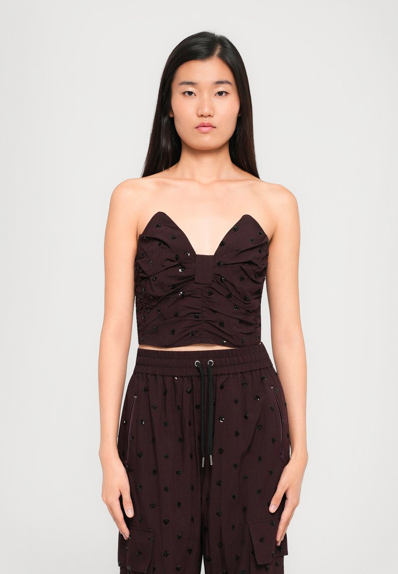 Burgundijska uska majica s dubokim V-izrezom, naboranom teksturom i ukrasima od crnih perlica, u kombinaciji s odgovarajućim hlačama koje imaju slične detalje.