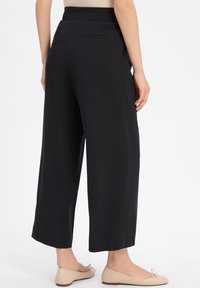 Black wide-leg pants made from soft fabric, featuring a elastic waistband and two back pockets. Smooth texture with a relaxed fit.