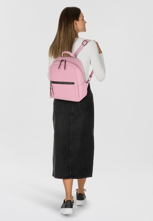Sac à dos rose clair de forme arrondie, avec double zip et poche avant. Matériau texturé, bretelles réglables et design minimaliste.