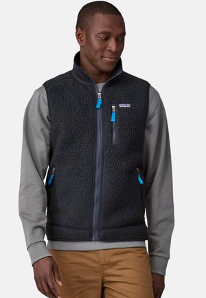 Black fleece vest with a textured surface, zippered pockets, and bright blue zippers. Worn over a gray long-sleeve shirt.