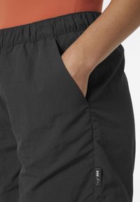 Černé lehké kalhoty s elastickým pasem, bočními kapsami a malou nášivkou na levé straně, která zobrazuje logo značky.