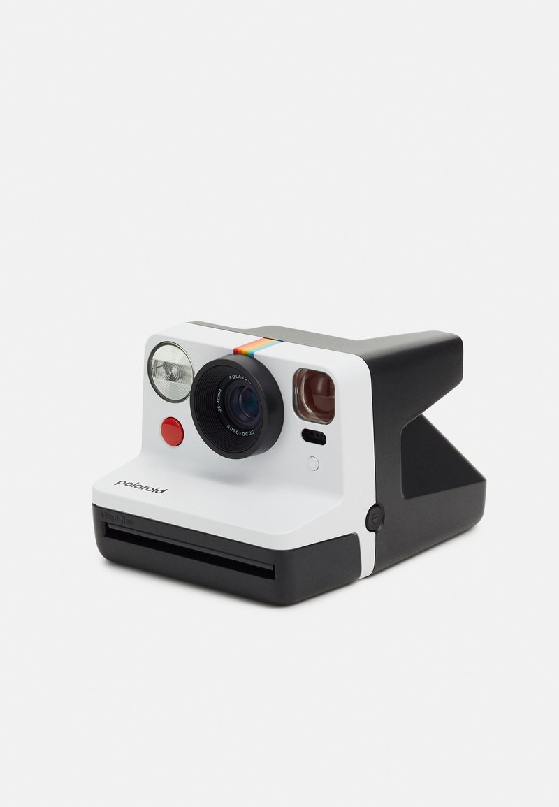 Appareil photo instantané Polaroid avec une façade blanche, une base noire, un objectif circulaire, un bouton rouge et une bande arc-en-ciel en accent. Forme compacte et rectangulaire.