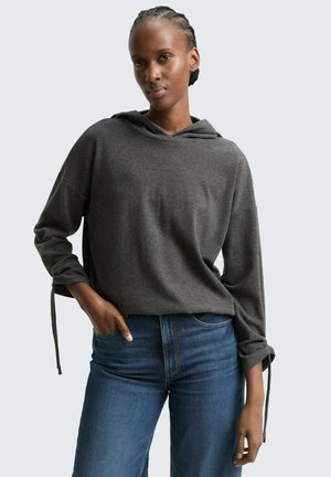 Grauer Kapuzenpullover mit langen Ärmeln und gebundenen Manschetten, kombiniert mit blauen gerade geschnittenen Jeans. Glatte Textur und entspannter Schnitt.
