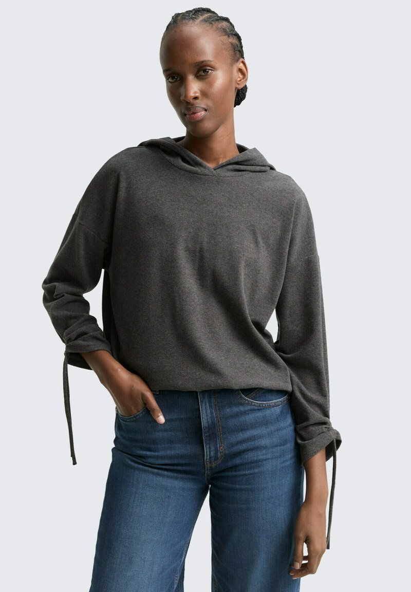Grijze hoodie met lange mouwen en gestrikte manchetten, gecombineerd met blauwe rechte jeans. Soepele textuur en relaxte fit.