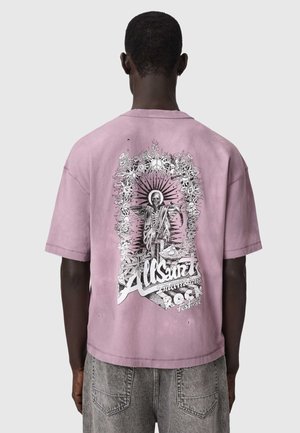 Bărbat purtând un tricou lavandă lejer cu o grafică alb-negru cu schelet și textul „AllSaints International Rock Festival” pe spate.