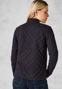 Veste matelassée bleu foncé avec un col haut, présentant un motif géométrique en losanges, un tissu texturé et une coupe ajustée.