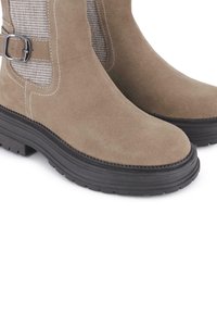 Botas de tobillo de ante marrón con paneles laterales elásticos, suela gruesa de goma negra y un detalle decorativo de hebilla en el lateral.