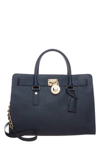 Sac à main en synthétique bleu marine avec finition texturée, doubles poignées, accessoires en métal doré, bandoulière réglable et un charme logo attaché.