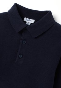 Polo shirt lavorato a maglia di colore navy con colletto classico, apertura con tre bottoni e texture morbida, con un'etichetta che mostra il nome del marchio all'interno.