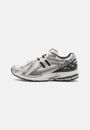 Chaussure de course New Balance blanche et argentée avec des accents noirs, dessus en mesh, semelle amortie et le logo "N" sur le côté.