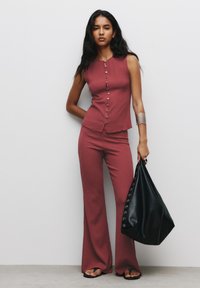 Rosa tvådelad set med ärmlös topp med knappar och utsvängda byxor. Svart läderväska med detaljer i öglor och platta sandaler.