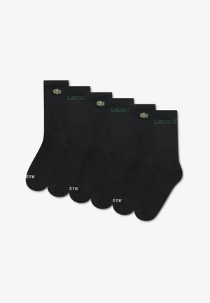 Ensemble de cinq chaussettes en coton noir avec une texture côtelée, le logo Lacoste vert et le texte blanc « LACOSTE » sur la zone des orteils.