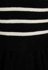 Svart stickad tyg med horisontella vita ränder. Texturen är ribbad, med en utsvängd design under den randiga sektionen.