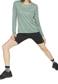 Langärmliges mintgrünes Sportoberteil kombiniert mit schwarzen Kompressionsshorts, ausgestattet mit einem figurbetonten Design und strukturiertem Stoff. Schwarze Sneakers runden den Look ab.