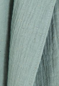 Tissu tissé bleu clair présentant une texture légèrement froissée et de petites paillettes dorées. Tissu doux, respirant et léger.
