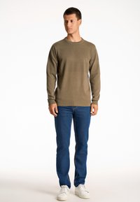 Maglione lavorato a maglia verde oliva con motivo testurizzato, collo rotondo e polsini a coste. Abbinato a jeans in denim blu e sneakers bianche.