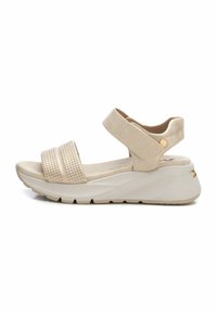 Sandalias de cuña beige con tiras perforadas, correa de tobillo ajustable y suela texturizada. Material suave con acabado liso. Detalle en dorado.